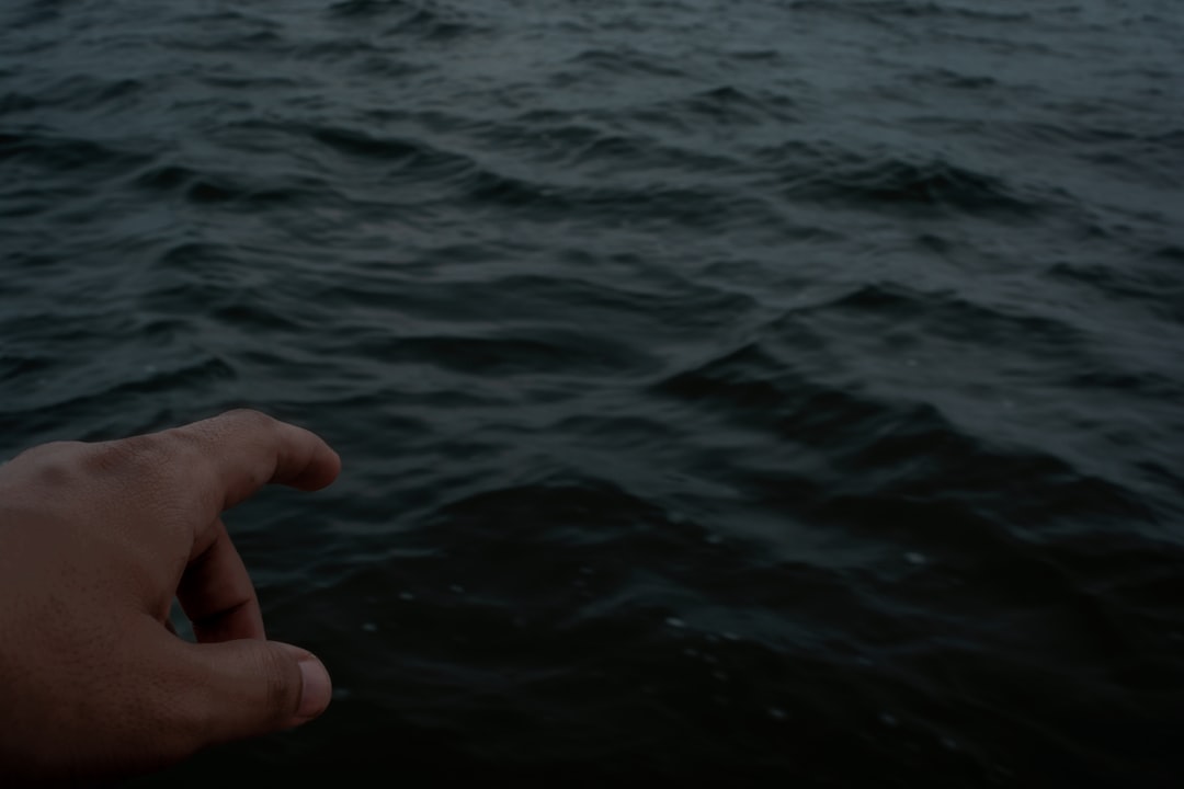 a person's hand pointing towards the water